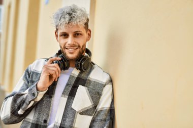 Şehirde kulaklık takarak mutlu gülümseyen genç İspanyol adam..