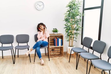 Ortadoğulu genç bir kadın bekleme odasında oturmuş müzik dinliyor.