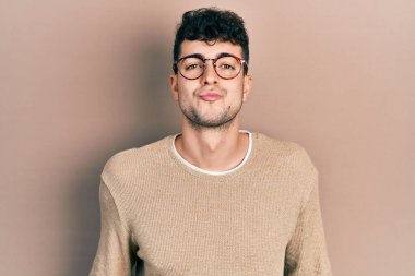 Latin asıllı genç bir adam, günlük kıyafetler ve gözlüklerle kameraya bakıyor. Havada öpücük yolluyor. Sevimli ve seksi. aşk ifadesi. 