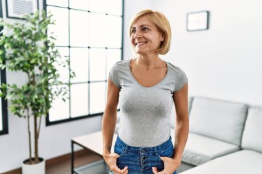 Orta yaşlı sarışın kadın, gülümsüyor.