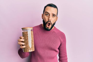 Sakallı genç adam elinde sağlıklı tahıl gevreği kavanozu tutuyordu. Korktu ve şaşırdı. Ağzı açık kaldı. 