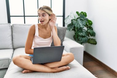 Genç sarışın kadın evinde dizüstü bilgisayar kullanıyor. Kanepede oturuyor. Kulaktan kulağa gülümsüyor ve dedikoduları dinliyor. Sağırlık kavramı. 