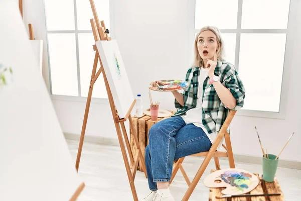 若いアーティストの女性の絵のキャンバスでアートスタジオ驚きと驚きの上を見て指と腕を上げて — ストック写真