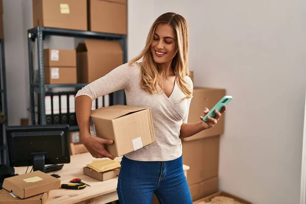 Young Blonde Woman Ecommerce Business Worker Using Smartphone Holding Package — Stock Photo, Image