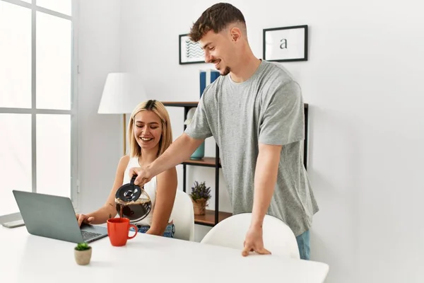 自宅でノートパソコンを使って仕事をしている女性と彼女のボーイフレンドがコーヒーを注ぐ — ストック写真