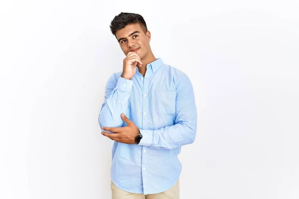 若いヒスパニック系の男性のビジネスシャツの質問については 集中的な表現を考えて手で孤立した背景の上に立って着ている 笑顔で思いやりのある顔 疑わしい概念 — ストック写真