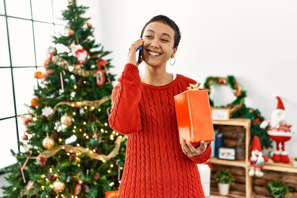 Jovem Hispânica Falando Smartphone Segurando Presente Junto Árvore Natal Casa — Fotografia de Stock