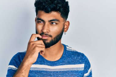 Sakallı, normal çizgili tişörtlü, ciddi yüzlü, eli çeneli, kafa karıştırıcı bir fikir hakkında soru soran bir Arap. 