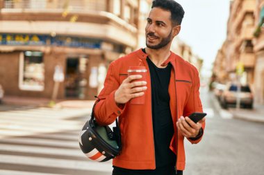 Genç İspanyol adam akıllı telefon kullanıyor. Şehirde kahve kaskı içiyor..