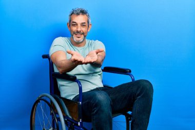 Tekerlekli sandalyede oturan, elleri avuçlarında gülümseyen ve el hareketi yapan orta yaşlı yakışıklı bir adam. Bekleme ve koruma 