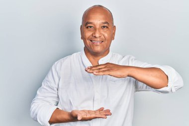 Orta yaşlı, gündelik kıyafetler giyen, büyük ve büyük beden işareti gösteren el kol hareketleri yapan Latin bir adam. Ölçü sembolü. Kameraya bakıp gülümsüyor. ölçüm kavramı. 