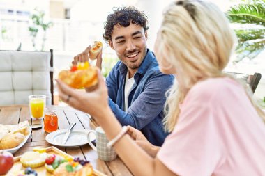 Genç çift, mutlu bir şekilde gülümsüyor. Kahvaltıyı terasta yapıyorlar..