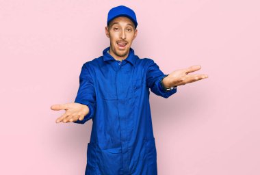 Sakallı, inşaatçı tulumu giyen, neşeli gülümseyen, yardım eli uzatan ve kabul gören kel bir adam.. 