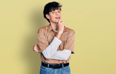 90 'ların retro tarzı giyinen yakışıklı hippi genç adam kameraya kollarını kavuşturmuş ve çenesine dokunmuş bir şekilde gülümsüyor. Olumlu düşünmek. 