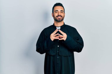 Sakallı, Katolik rahip cübbesi giymiş yakışıklı İspanyol bir adam ellerini kavuşturup gülümseyerek gevşemiş ve neşeli olmasını diliyordu. Başarı ve iyimserlik 