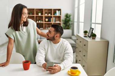 Genç Latin çift evde akıllı telefon kullanarak mutlu bir şekilde gülümsüyor..