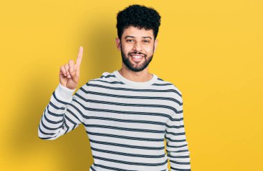 Sakallı, sıradan çizgili süveter giyen genç bir Arap başarılı bir fikri işaret ediyor. Heyecanlı ve mutlu. Bir numara.. 