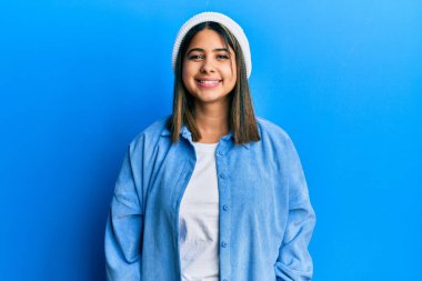 Yüzünde mutlu ve havalı bir gülümseme olan sevimli yün şapkalı genç Latin kadın. şanslı kişi. 