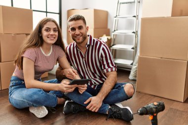 Yeni evimizde akıllı telefon kullanarak mutlu bir şekilde gülümseyen beyaz bir çift..