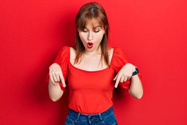 Kızıl saçlı, kırmızı tişörtlü genç bir kadın parmaklarını göstererek reklamı gösteriyor, şaşırmış bir yüz ve açık bir ağız. 