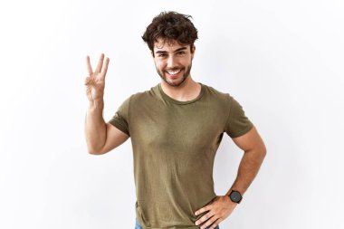 İzole edilmiş beyaz arka planda duran İspanyol adam üç numaralı parmaklarıyla gülümseyerek kendinden emin ve mutlu bir şekilde işaret ediyor.. 