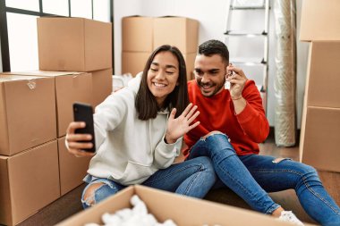 Genç Latin çift gülümsüyor. Yeni evlerinde akıllı telefon kullanarak video araması yapıyorlar..