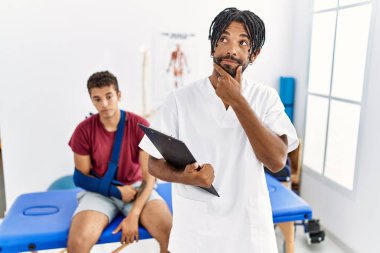 Kırık kollu bir adamla birlikte acı dindirme kliniğinde çalışan genç İspanyol adam kameraya kollarını kavuşturup gülümsüyor ve çenesini kaldırıyor. Olumlu düşünmek. 