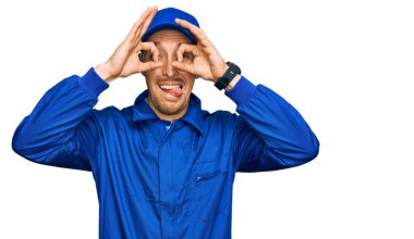 Sakallı, inşaatçı tulumu giymiş, kel bir adam. Dürbün gibi güzel hareketler yapıyor. Dürbün dilini çıkarıyor, gözler parmaklarından bakıyor. çılgın ifade. 