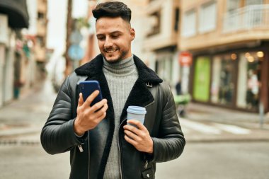 Genç Arap adam akıllı telefon kullanıyor ve şehirde kahve içiyor..