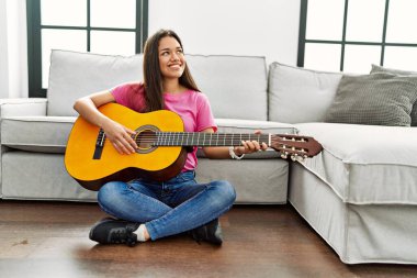 Genç Latin kadın klasik gitar çalıyor. Evde yerde oturuyor.