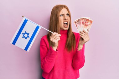 Genç İrlandalı kadın İsrail bayrağını tutuyor ve şekeller para basıyor kızgın ve öfkeli çığlıklar atıyor öfkeyle bağırıyor. öfke ve agresif konsept. 
