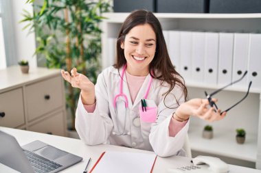 Klinikte doktor üniforması giyen genç bir kadın konuşuyor.