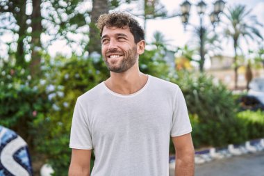 Genç İspanyol adam parkta yürürken kendinden emin gülümsüyor.