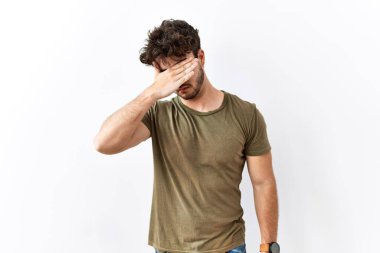 Hispanik adam izole edilmiş beyaz arka planda duruyor. Gözleri elle örtüyor, ciddi ve üzgün görünüyor. Görme, saklama ve reddetme konsepti 