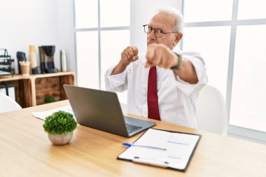 Ofiste çalışan kıdemli bir adam bilgisayarla dövüşmek için yumruk sallıyor agresif ve öfkeli saldırı, tehdit ve şiddet. 