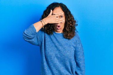 Orta yaşlı İspanyol kadın gündelik giysiler giymiş. Şoka girmiş. Yüzü ve gözlerini kapamış, utanmış ifadesiyle parmaklarından bakıyor.. 