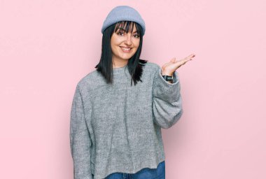 Şirin yün şapkalı genç İspanyol kadın neşeli bir şekilde gülümsüyor ve avuç içi kameraya bakıyor.. 