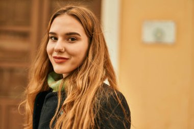 Genç sarışın kız gülümsüyor, mutlu bir şekilde şehirde duruyor..