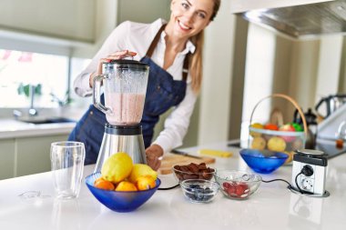 Genç sarışın kadın gülümsüyor. Kendine güveni tam. Smoothie 'yi sıvılaştırıyor.