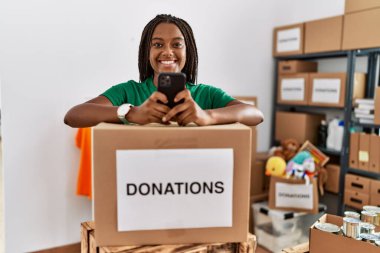 Genç Afrikalı Amerikalı kadın gönüllü üniforması giyiyor hayır kurumunda akıllı telefon kullanıyor.