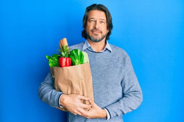 Orta yaşlı yakışıklı bir adam, elinde torbayla market alışverişi yaparken düşünceli, aklı başında ve kendine güvenen bir adam. 