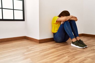 Genç bir kadın boş odada yerde oturup ağlıyor.