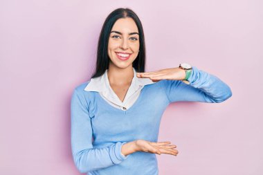 Pembe arka planda duran mavi gözlü güzel bir kadın. Elleriyle büyük ve büyük bir işaret, ölçü sembolü gösteriyor. Kameraya bakıp gülümsüyor. ölçüm kavramı. 