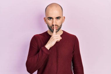 Gündelik kıyafetler giyen genç kel adam parmakları dudaklarında sessiz olmak istiyor. sessizlik ve gizli konsept. 