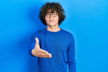 Yakışıklı, sıradan kıyafetler giyen ve gözlüklü bir genç. Dostça gülümseyen bir şekilde el sıkışarak hoş geldin diyor. başarılı iş. 