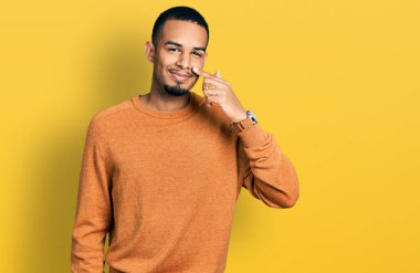 Genç Afro-Amerikan adam, günlük kıyafetler giyip, el ve burunla işaret ederek, neşeyle gülümsüyor. güzellik konsepti 