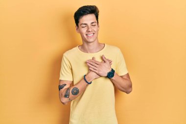Gündelik sarı tişört giyen genç İspanyol adam elleri göğsünde, gözleri kapalı ve yüzünde minnet dolu bir jest ile gülümsüyor. sağlık kavramı. 