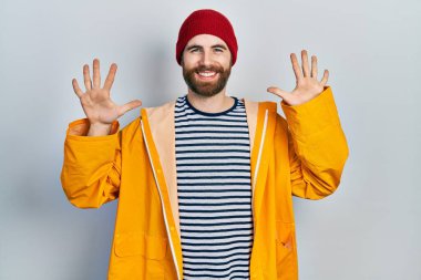 Sakallı, sarı yağmurluk giyen beyaz bir adam on numarayı gösterip işaret ederken kendinden emin ve mutlu bir şekilde gülümsüyor.. 