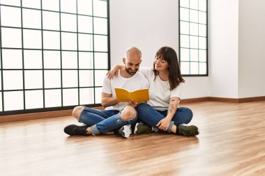 Genç İspanyol çift gülümsüyor boş evde mutlu bir kitap okuyor..