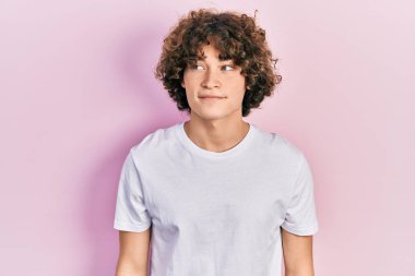 Yakışıklı, beyaz tişört giyen, gülümseyen, yan bakan ve düşünen genç bir adam.. 